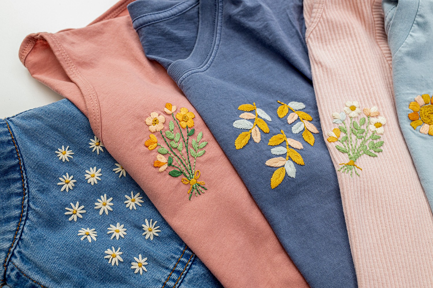 A row of clothing lies with embroidery designs stitched on top.