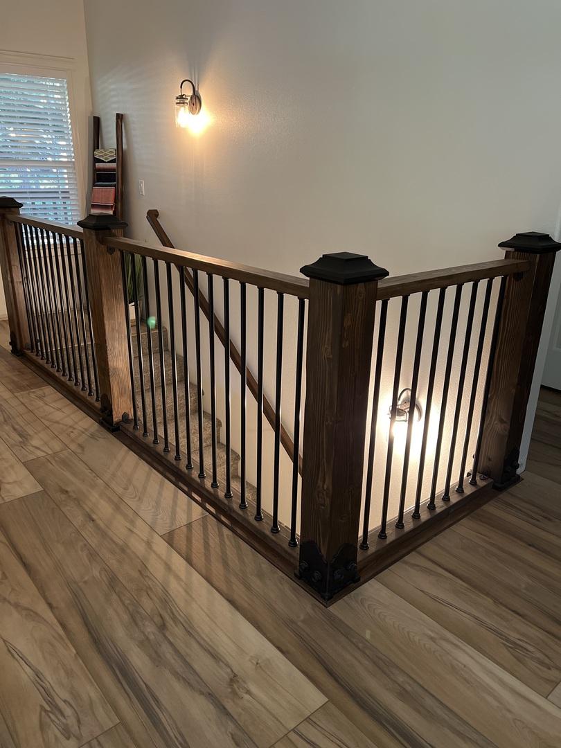 beautiful brown stained railing surrounding a stair well within the house. The railing is lined with black round snap'n lock balusters