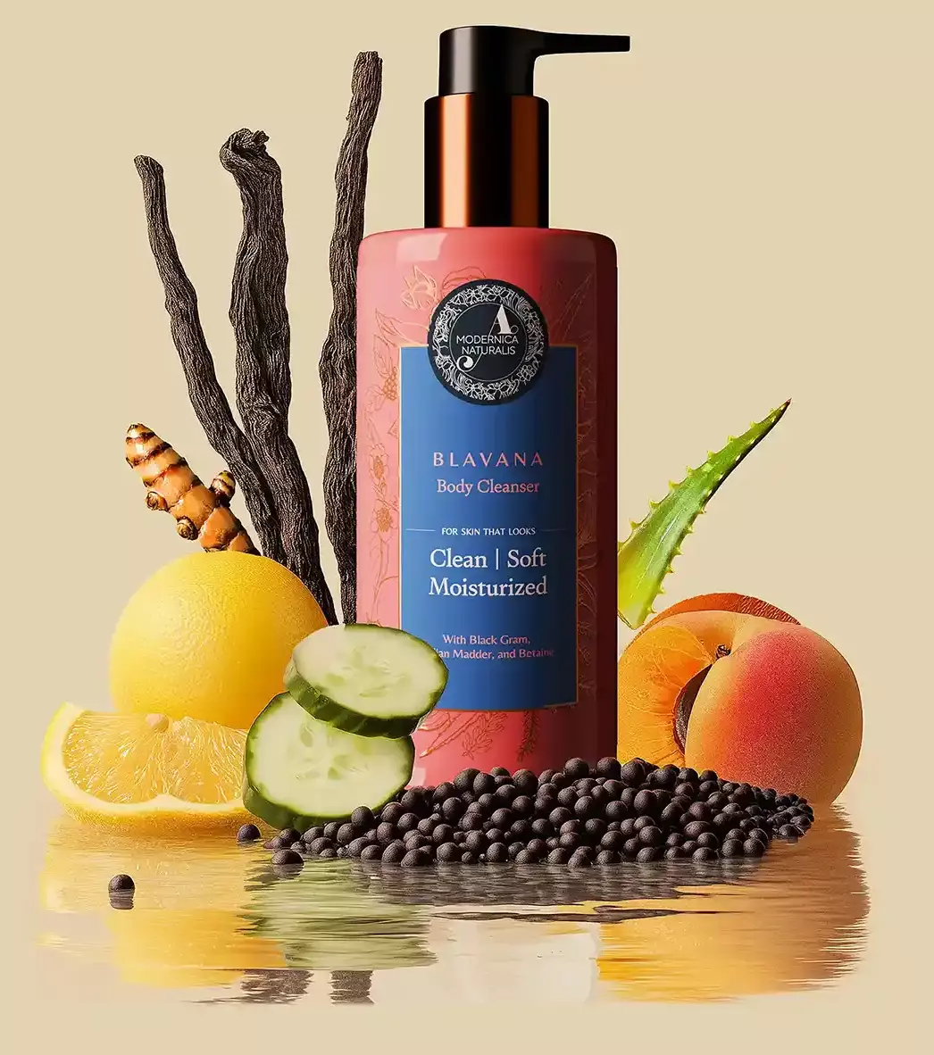 3. The image shows an arrangement of various natural ingredients around the blavana cleanser bottle. Ingredients include: A pink lotus flower Sliced lemons Whole lemons Cucumber slices Black gram manjistha sticks