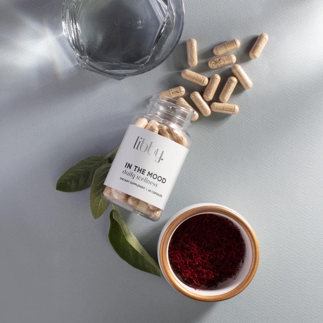 Bottle of Libby with capsules spilling out next to glass of water and bowl of saffron