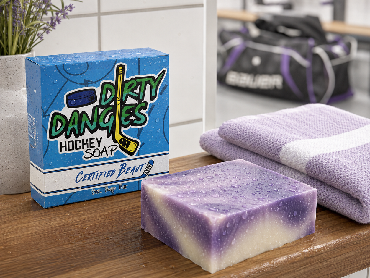 Certified Beaut hockey soap bar and box on a locker room bench beside a folded lavender towel with girl's hockey gear in the background.