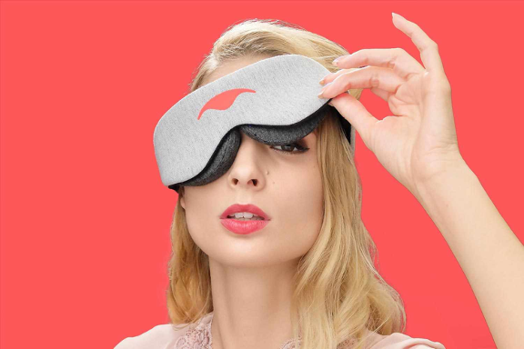 A girl lifting one corner of a sleep mask to show her eye.