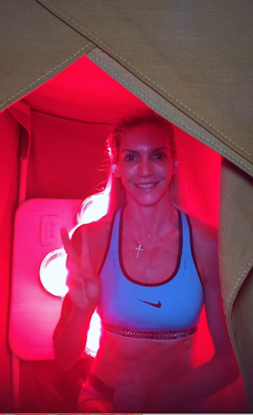 Smiling woman making peace sign inside red-lit sauna tent
