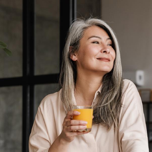 Person smiling in the kitchen and holding a glass of orange juice.