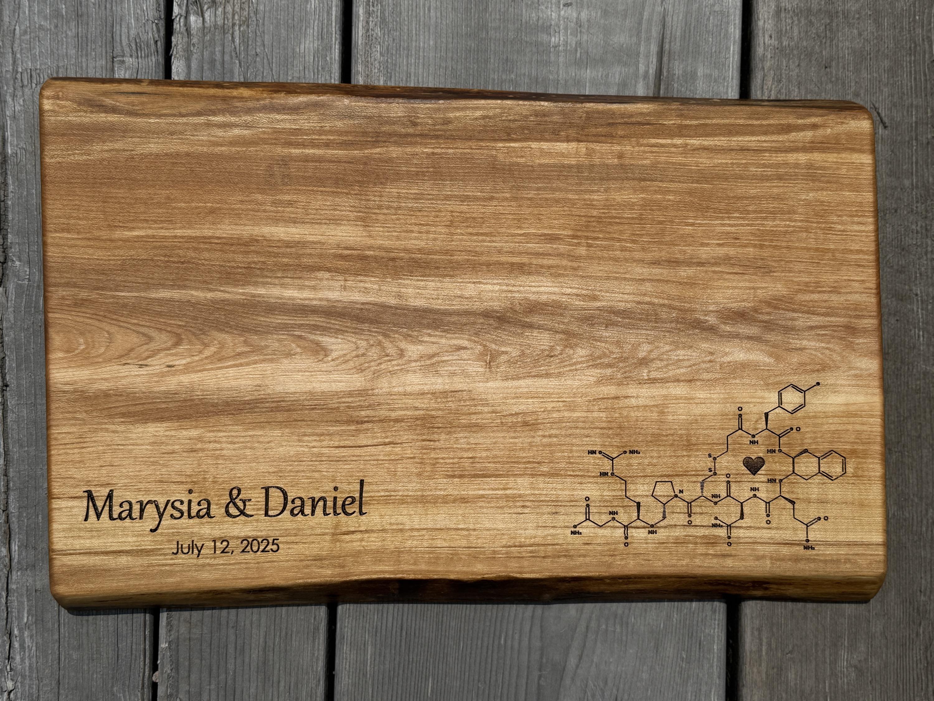 a maple live edge charcuterie board for a wedding gift featuring the molecular structure of oxytocin, often called the love hormone, paired with the couple’s names