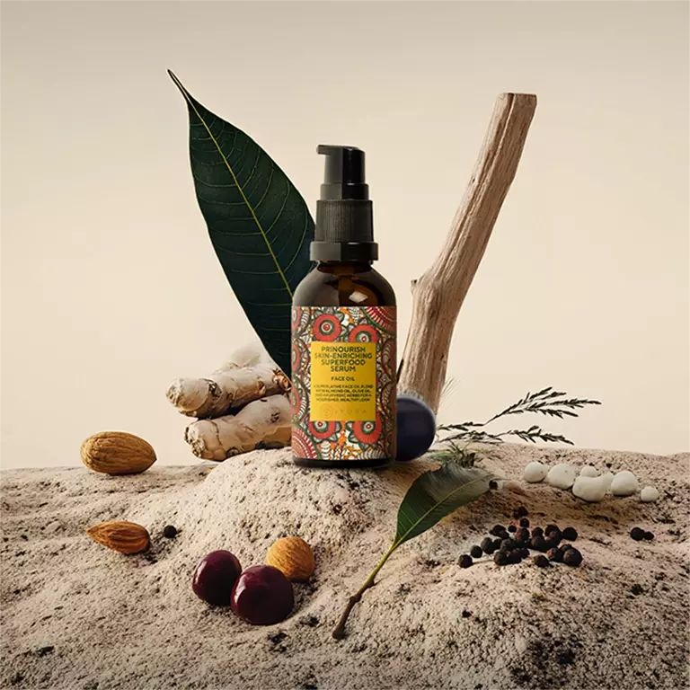A bottle of prinourish serum, with ingredients, like, almond, black pepper, black plum, ginger and more, kept on a rock