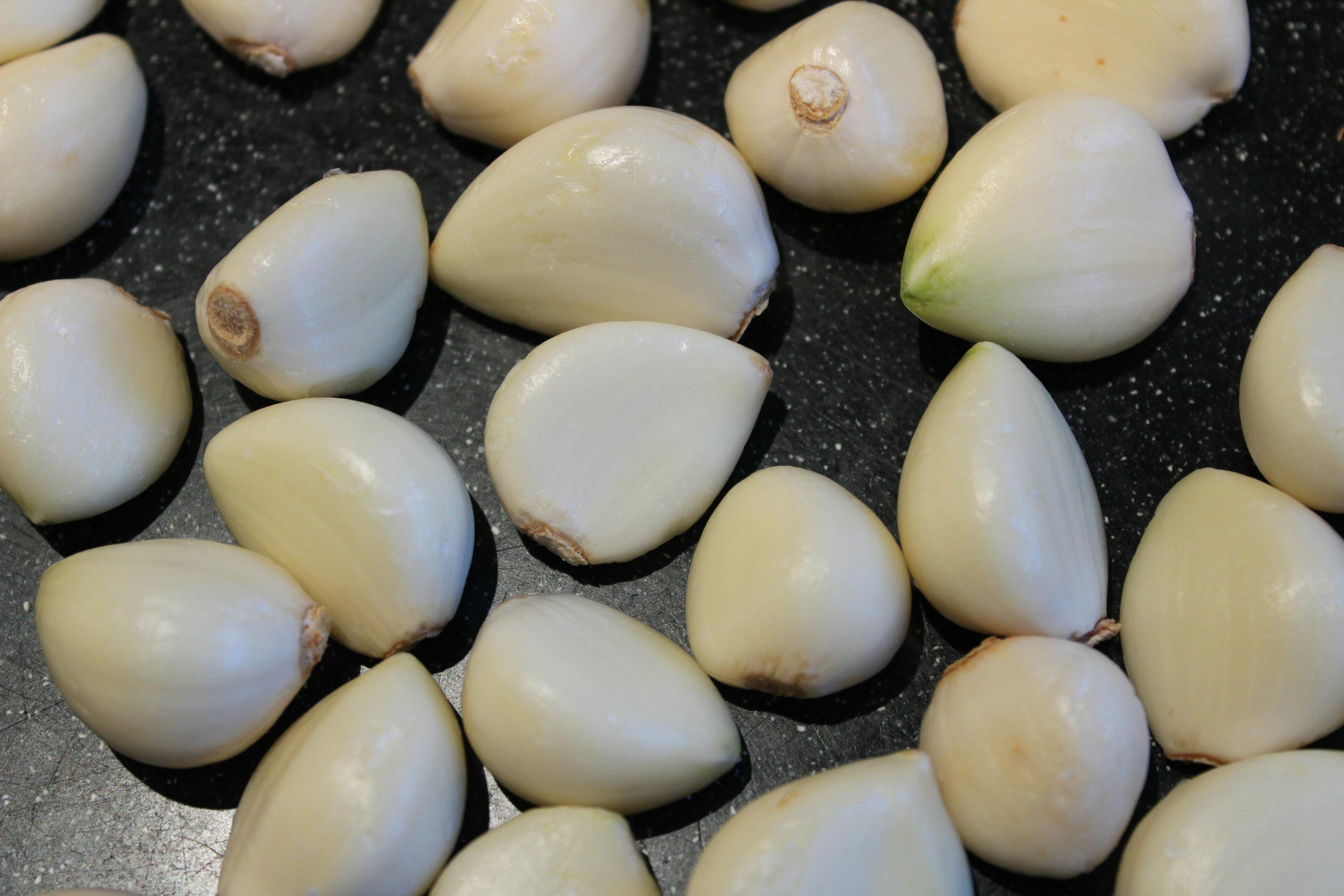 Close up image of several white cloves of garlic on a black table.
