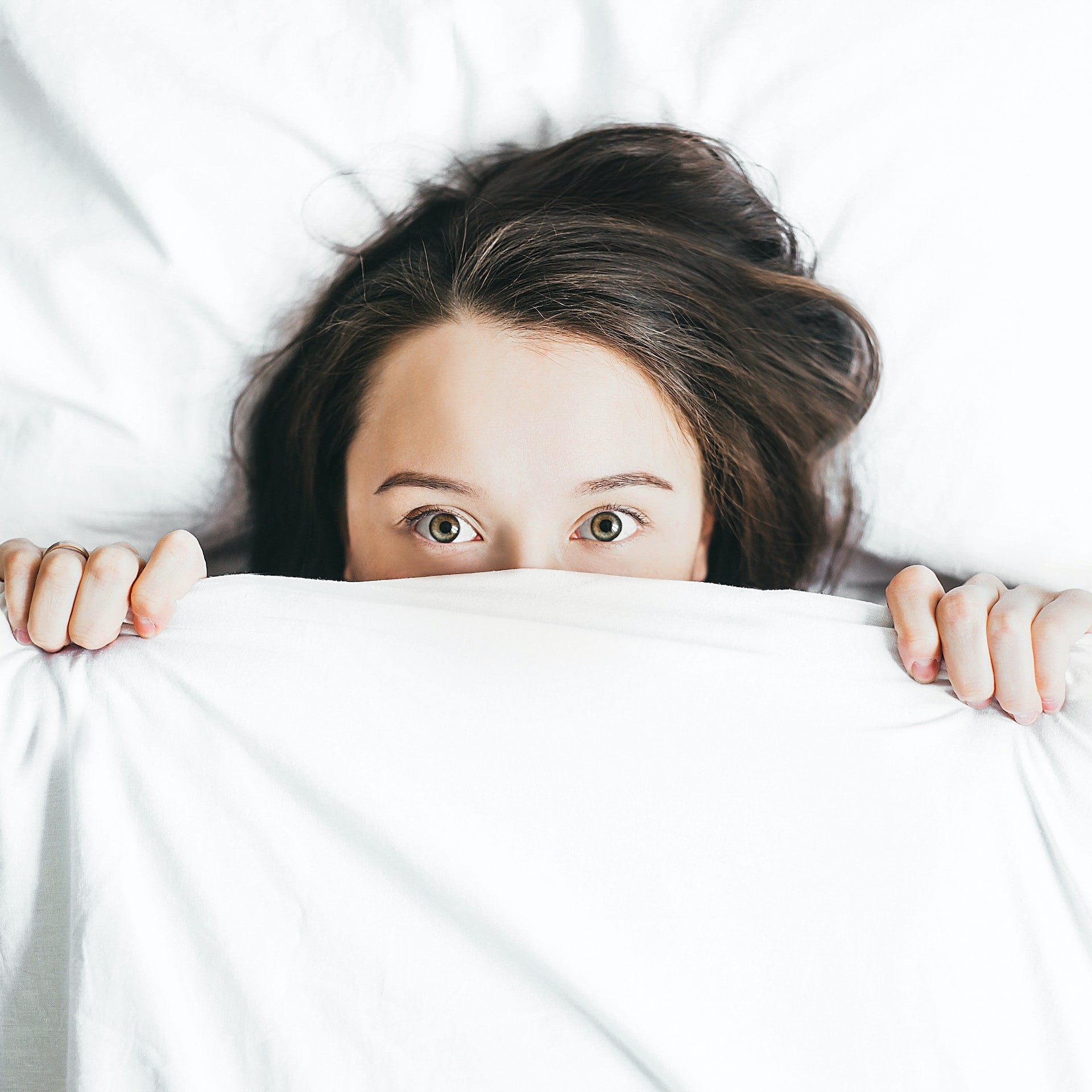 woman in bed with white duvet over her face