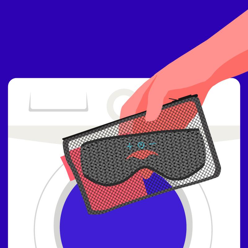 A hand placing a mesh laundry bag containing the straps and eye cups of a sleep mask with headphones into a washing machine.
