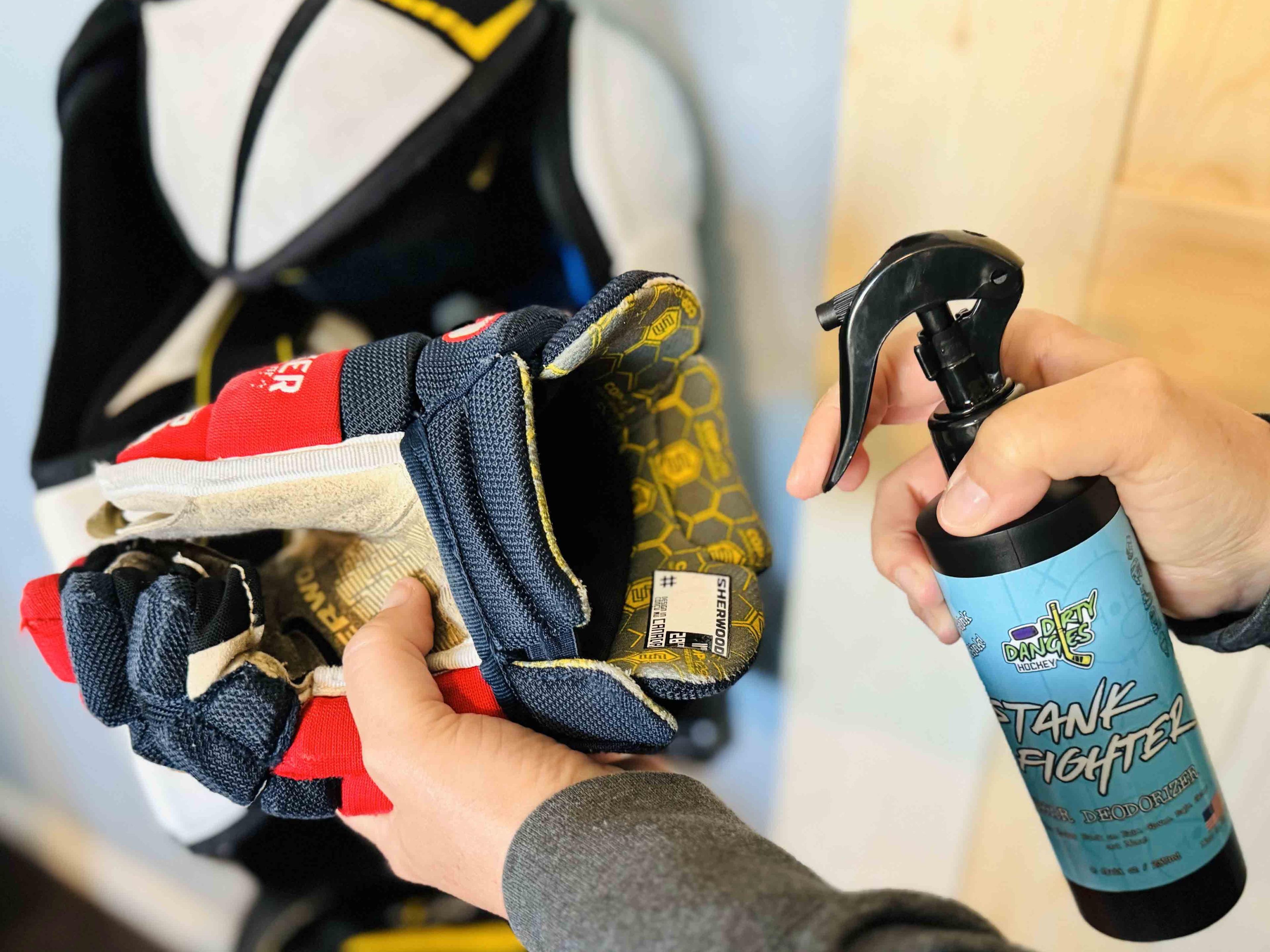A woman spraying a hockey glove with stank fighter deodorizing hockey spray