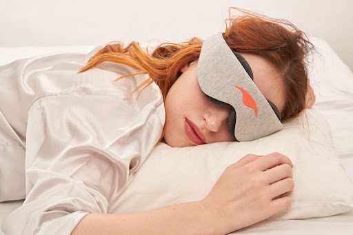 A redheaded girl sleeping on her tummy wearing a sleep mask with eye cups.