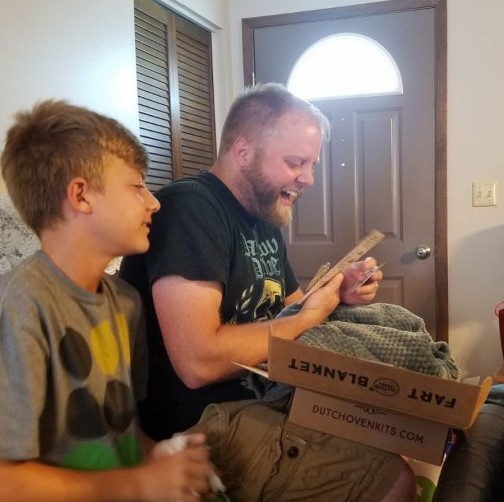 A dad smiles while opening a green dutch oven kit in front of his family