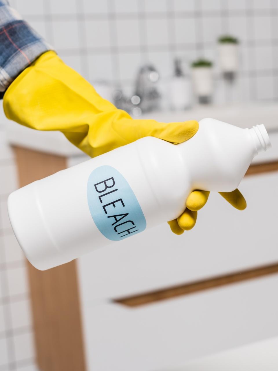 Cropped view of a hand holding bottle with bleach lettering in bathroom