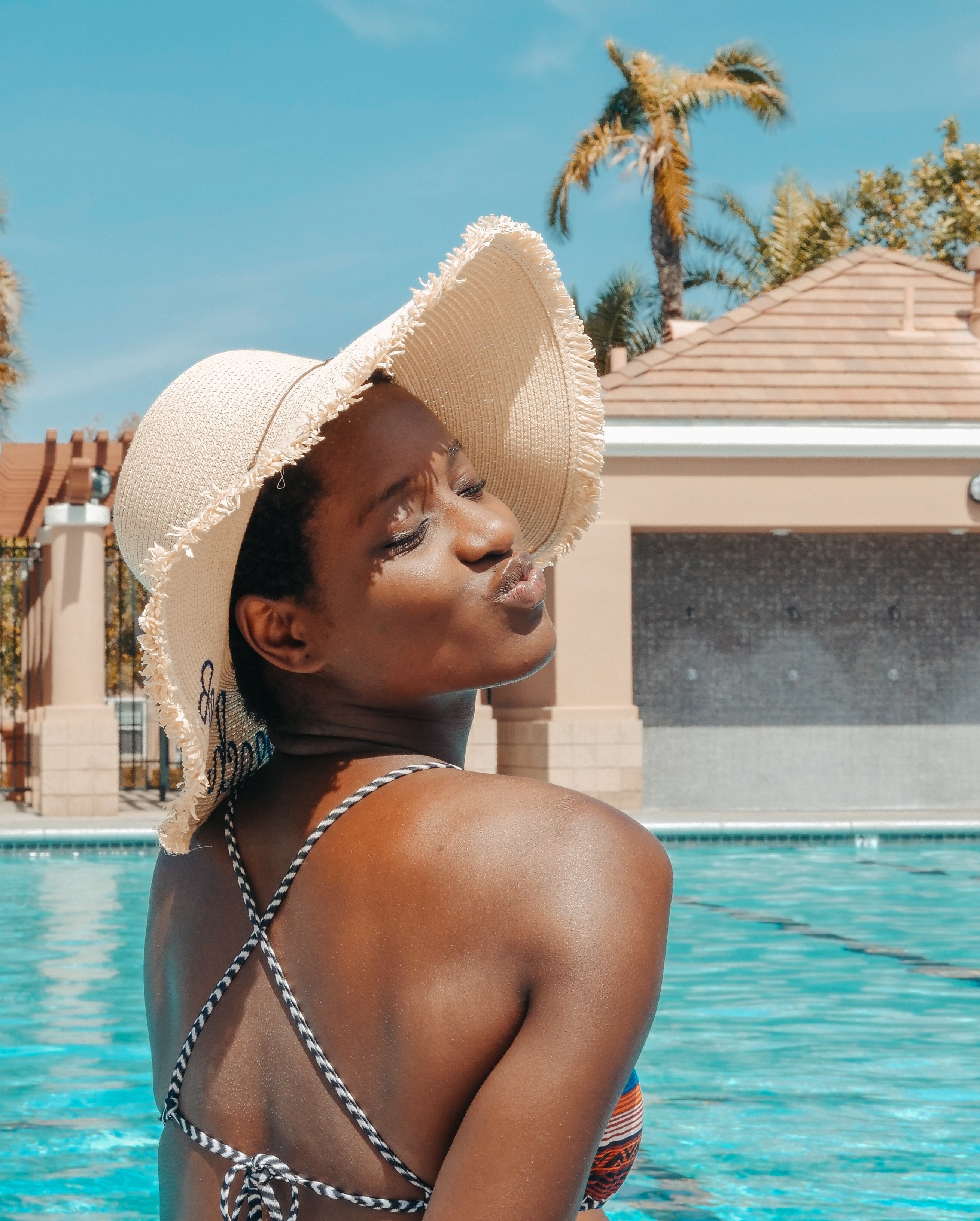 black woman with natural hair on vacation swimming at the pool in a sun hat and bathing suit