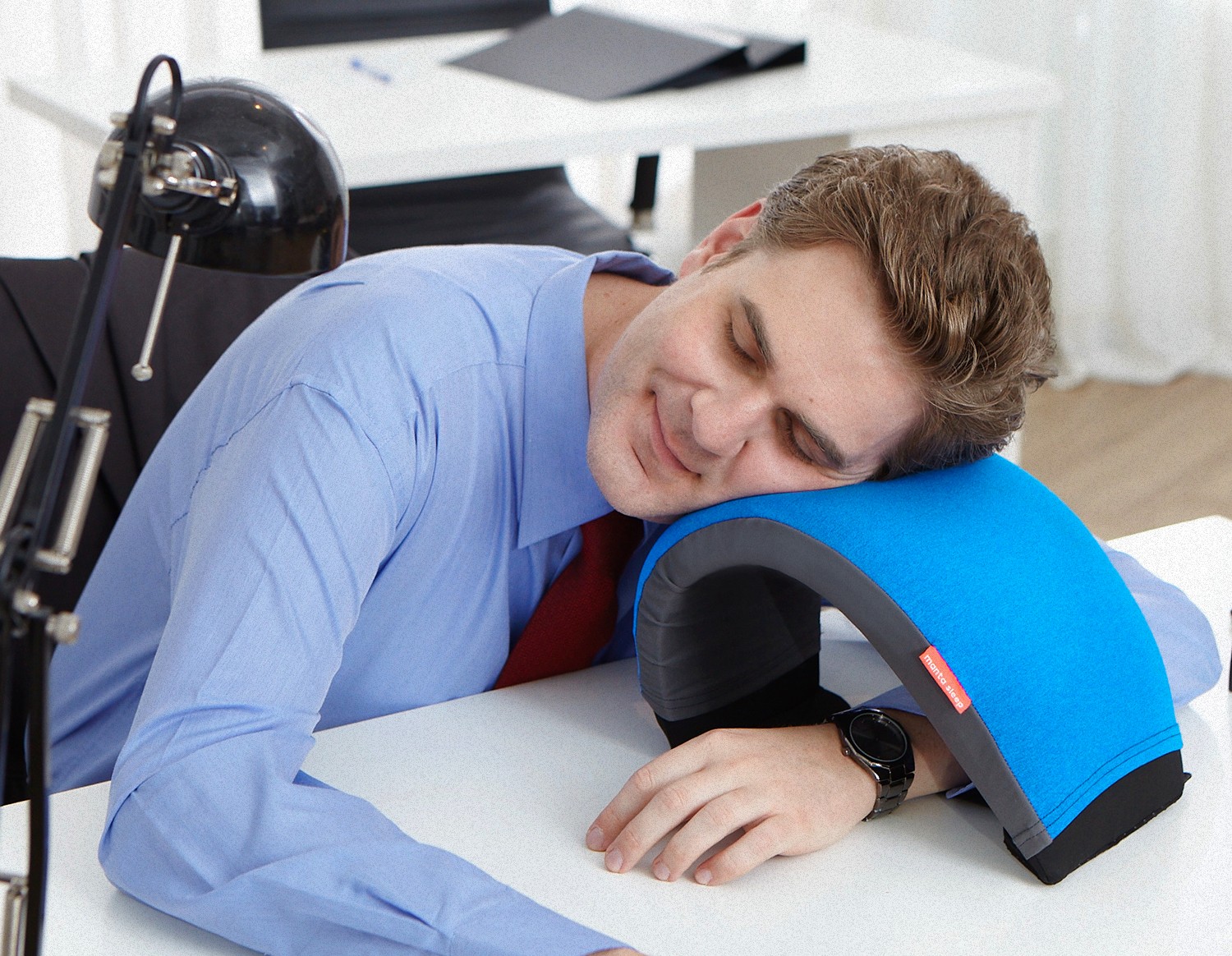 A man power napping on his work desk, using an arc-shaped blue nap.