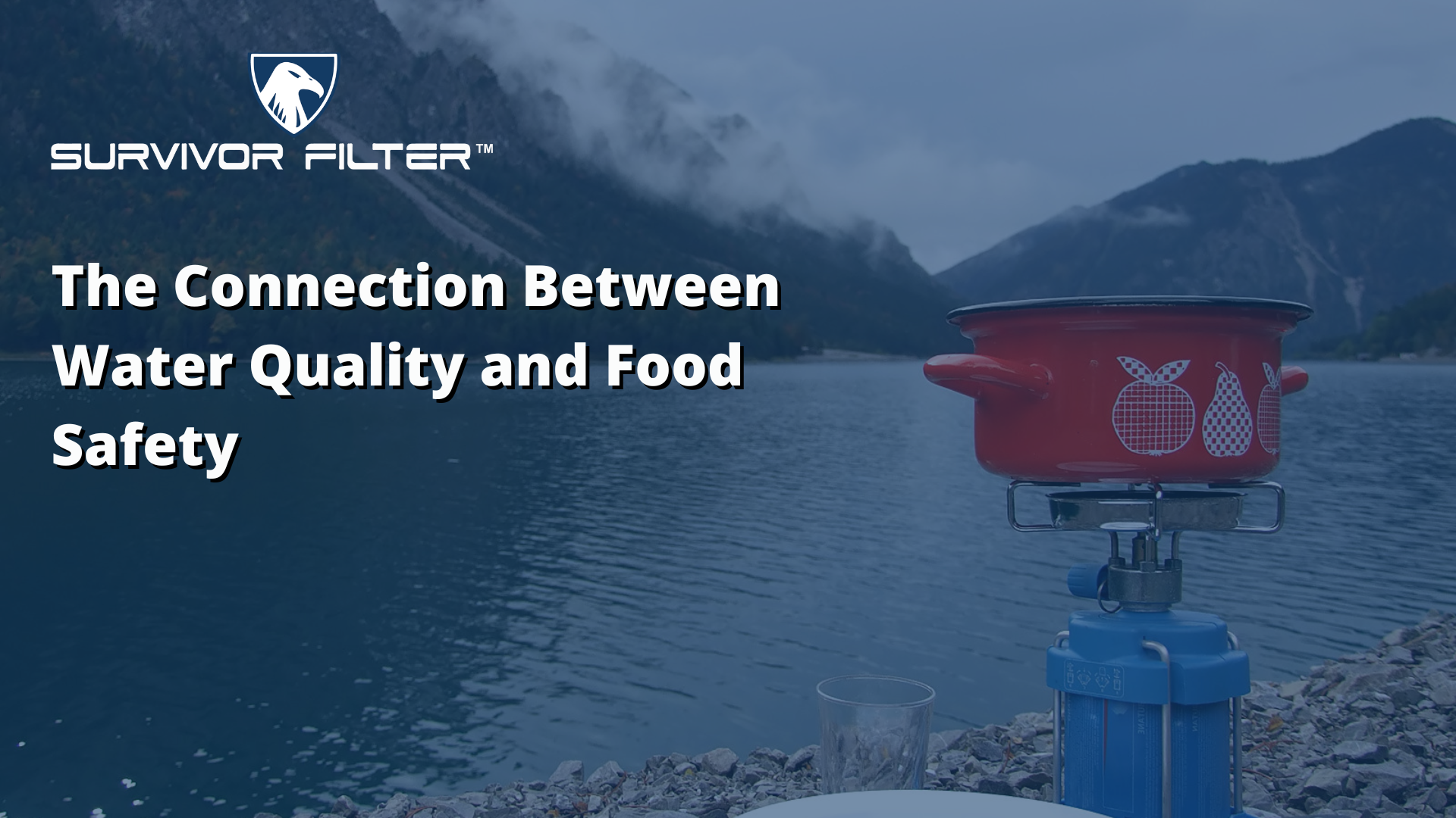 A pot on a gas cooker in front of a river with mountains in the background.