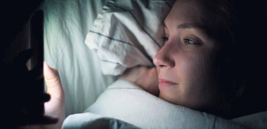Woman scrolling on her phone on her bed at night