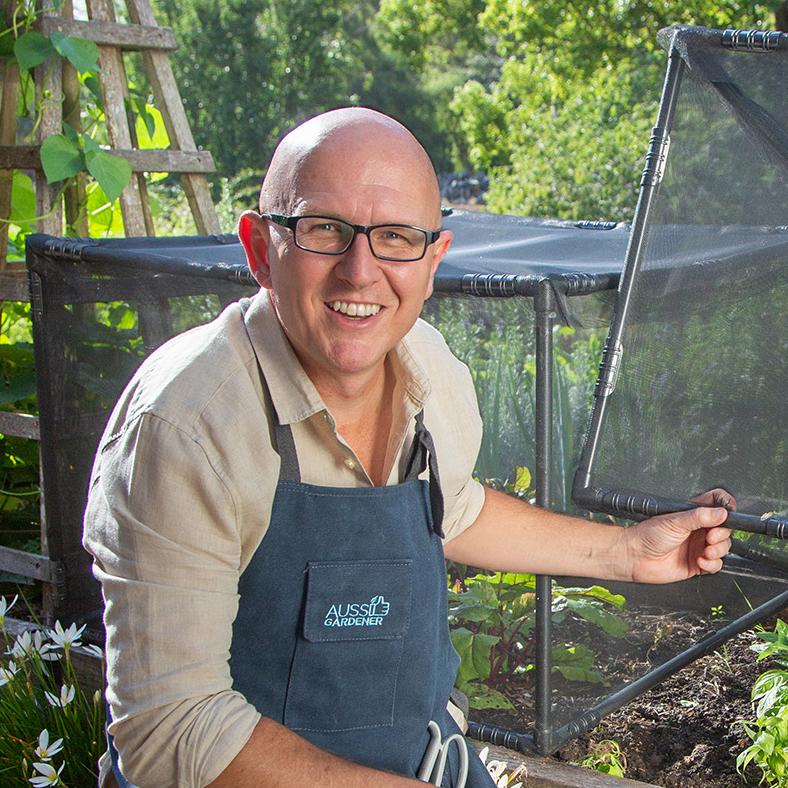Brian in a garden wearing an apron, opening a Pestfree plant cover.