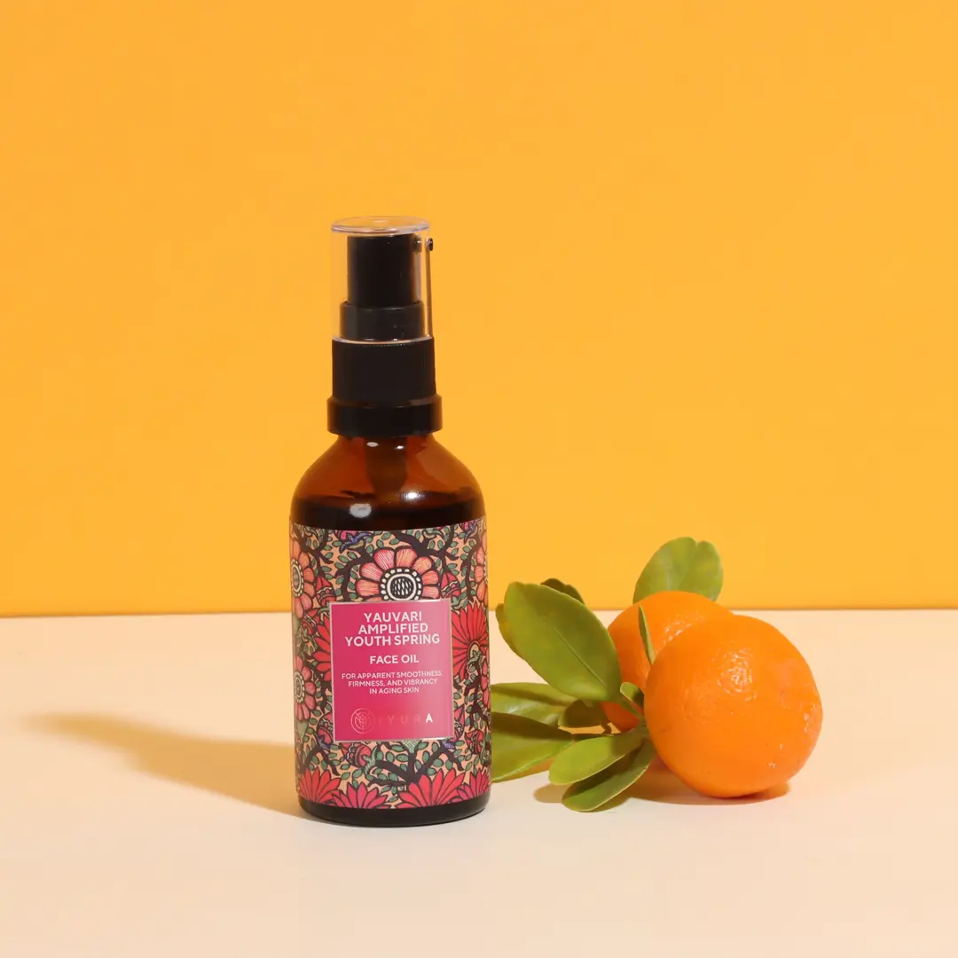 A bottle of Yauvari amplified youth spring and 2 limes with its leaves, kept in front of a yellow color background