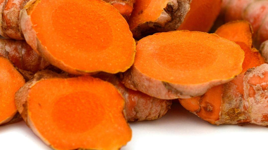 A pile of turmeric powder with 3 hunks of chopped turmeric root to the right of the pile