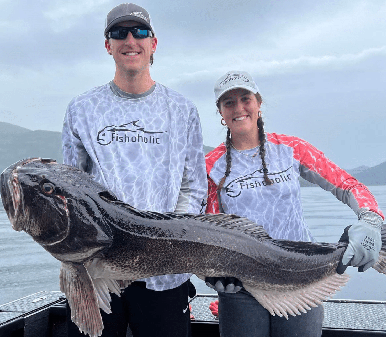 Man and woman holding up large fish wearing Fishoholic fishing shirts on a boat in the water