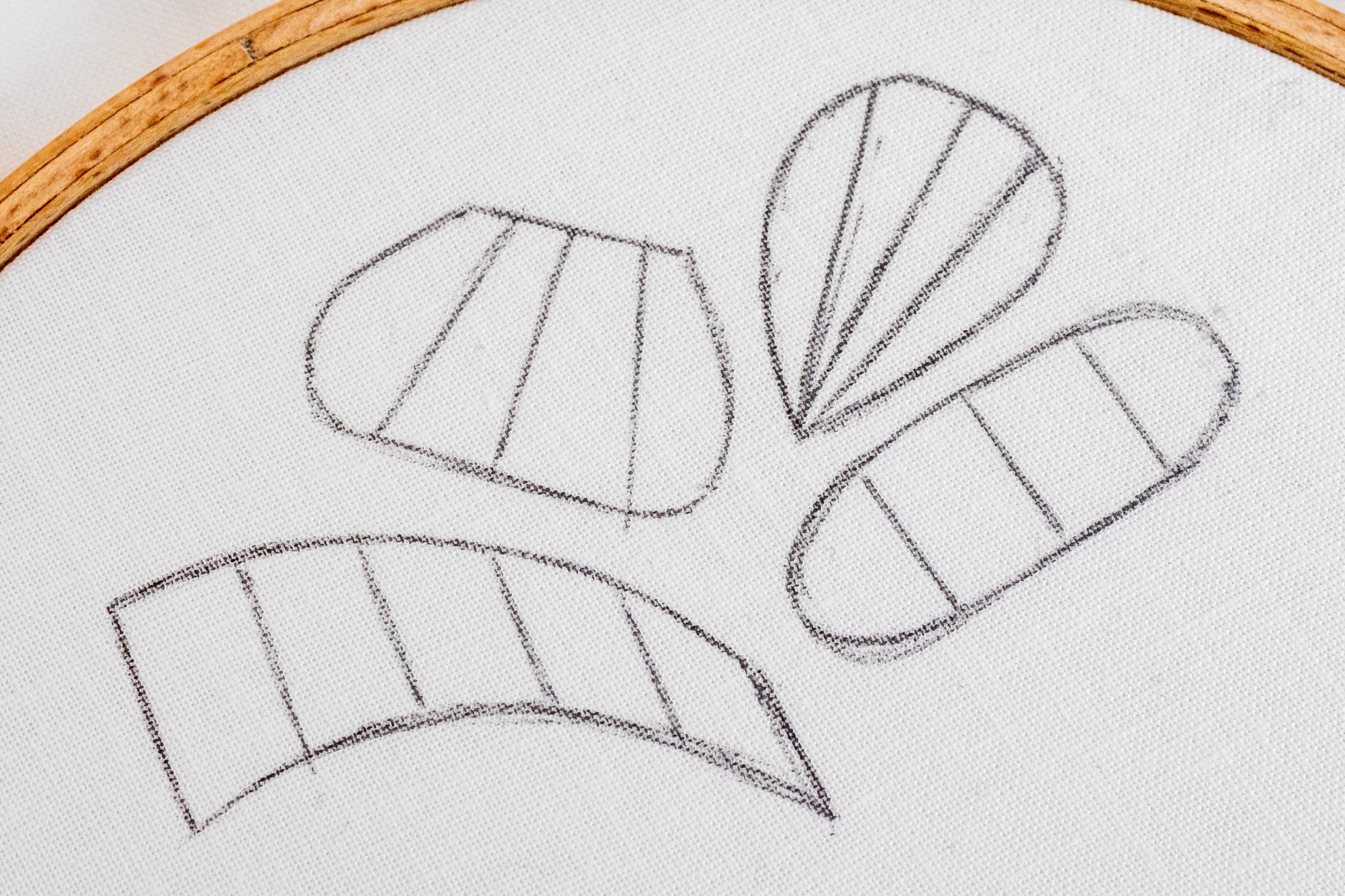Outlines of different satin stitch shapes with sectional/directional lines drawn on have been drawn on cotton fabric.