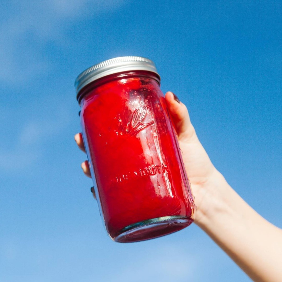 A mason jar filled with red smoothie held by a hand.