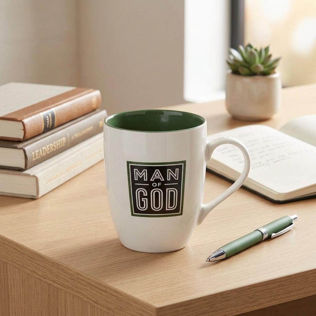 Man of God cactus green ceramic mug on a light wooden desk beside books and a green pen