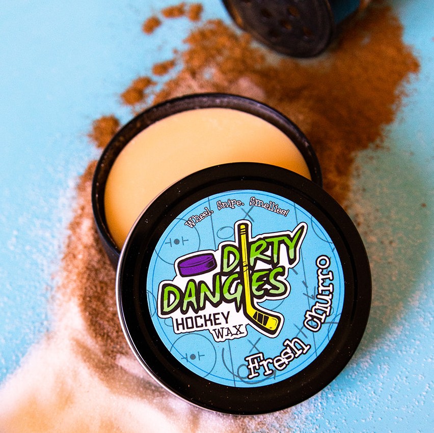 A tin of Dirty Dangles hockey stick wax sits on a blue background with cinnamon and sugar