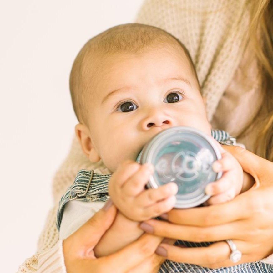 Baby being held and drinking from a glass baby bottle