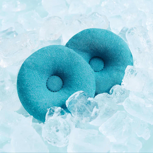 A pair of round, blue cooling eye cups for a sleep mask resting on ice cubes.