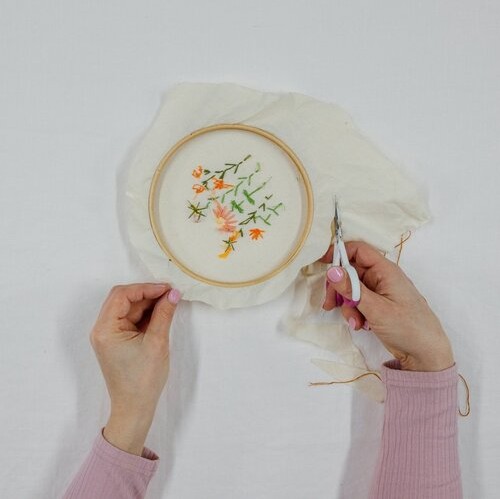 A hand cuts around the outside of the fabric, preparing to frame an embroidery creation.