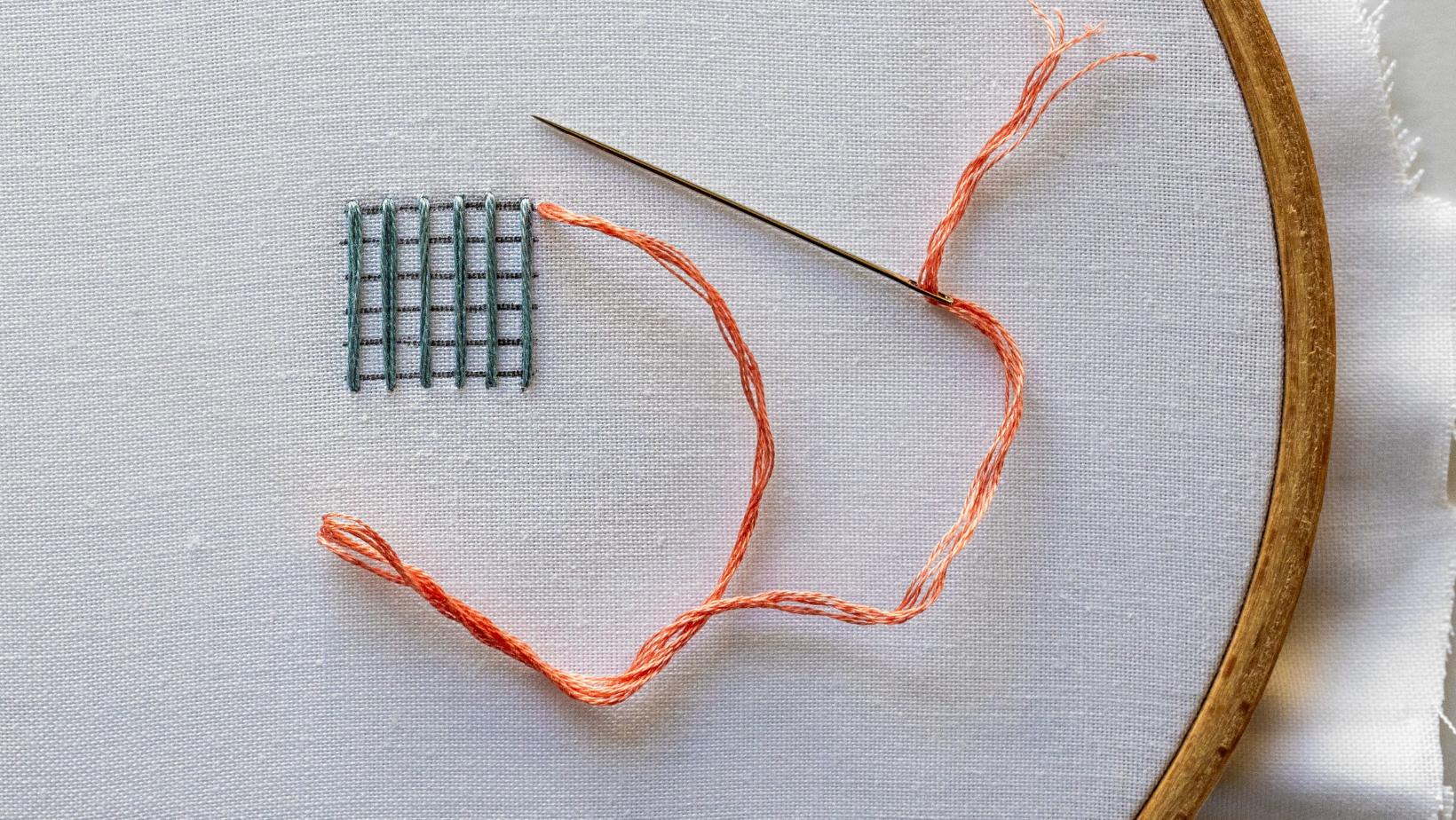 A needle coming up at the top right of the warp threads.