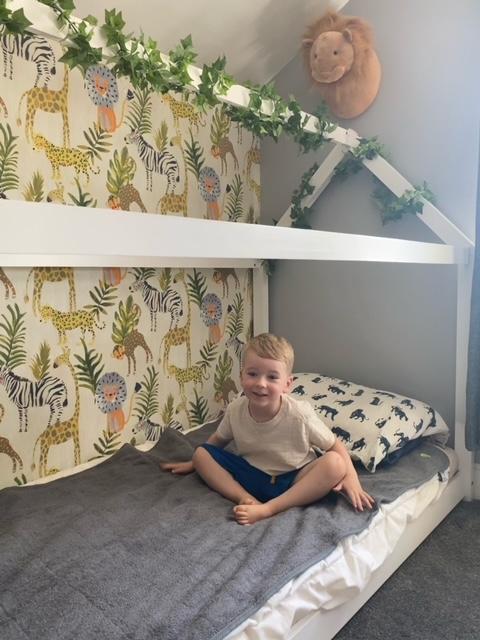 Toddler boy sitting on his bed with large grey PeapodMat - easy to look after washable bed mat.