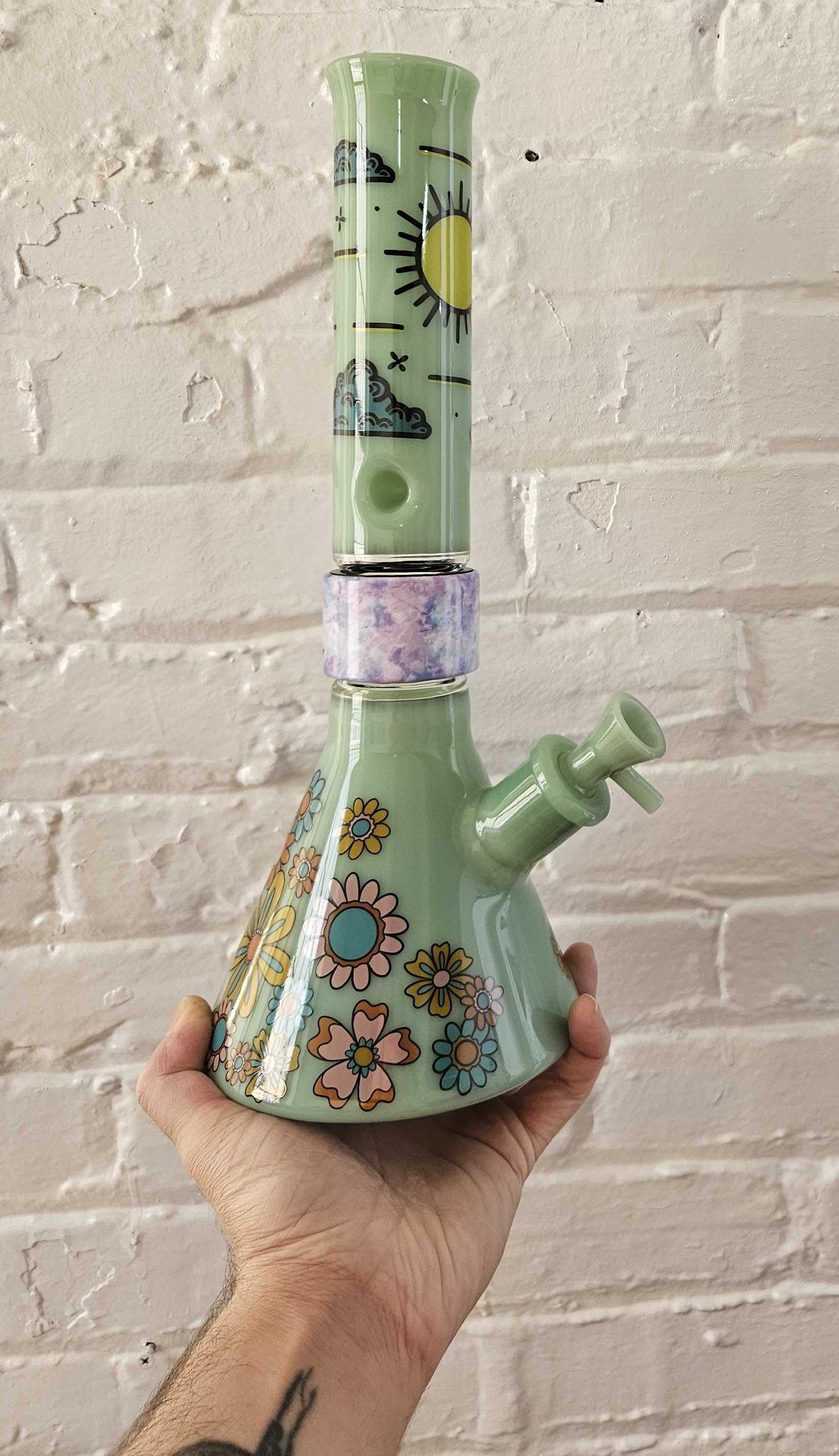 A custom Mint-colored Prism Beaker Bong Single Stack from our 3D builder. This modular setup features a clear beaker base with the Flower Power decal, a vibrant Tie Dye Halo connector, and a solid Mint glass mouthpiece with the Desert Dreamin' landscape decal.