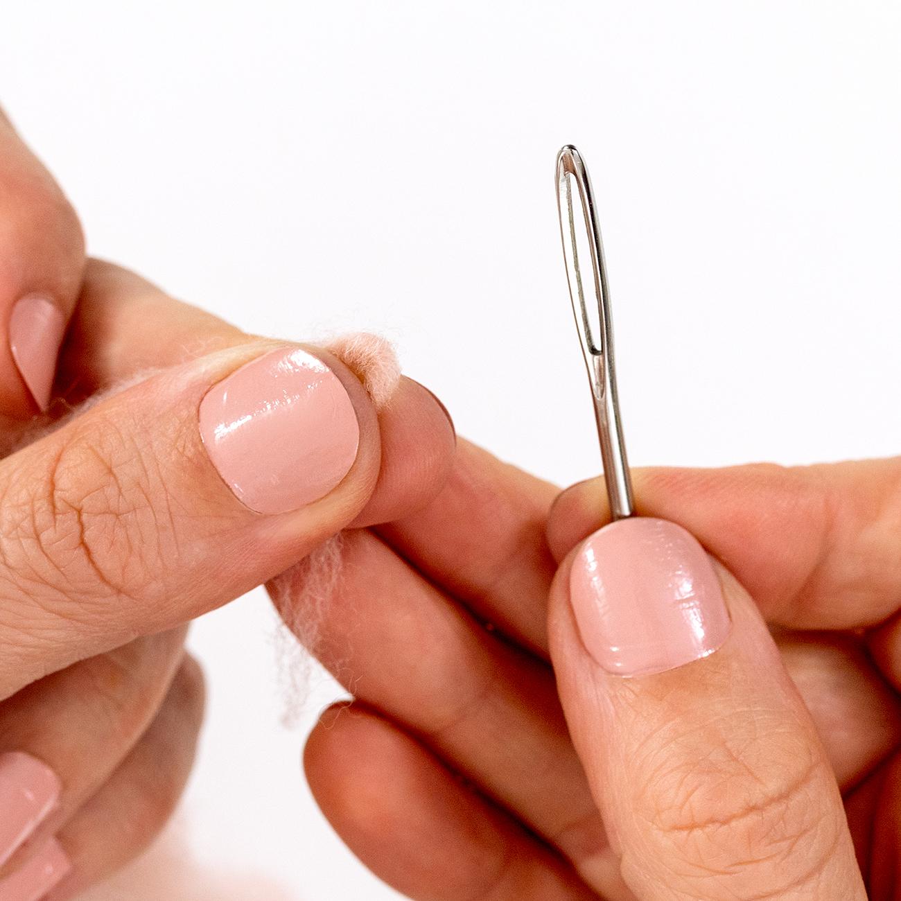 A hand holds a weaving needle and wool roving in another hand.