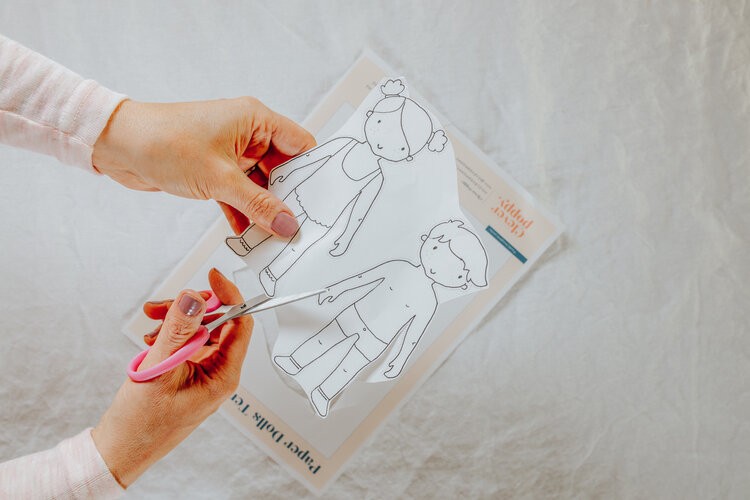 A hand cuts out paper dolls with scissors.