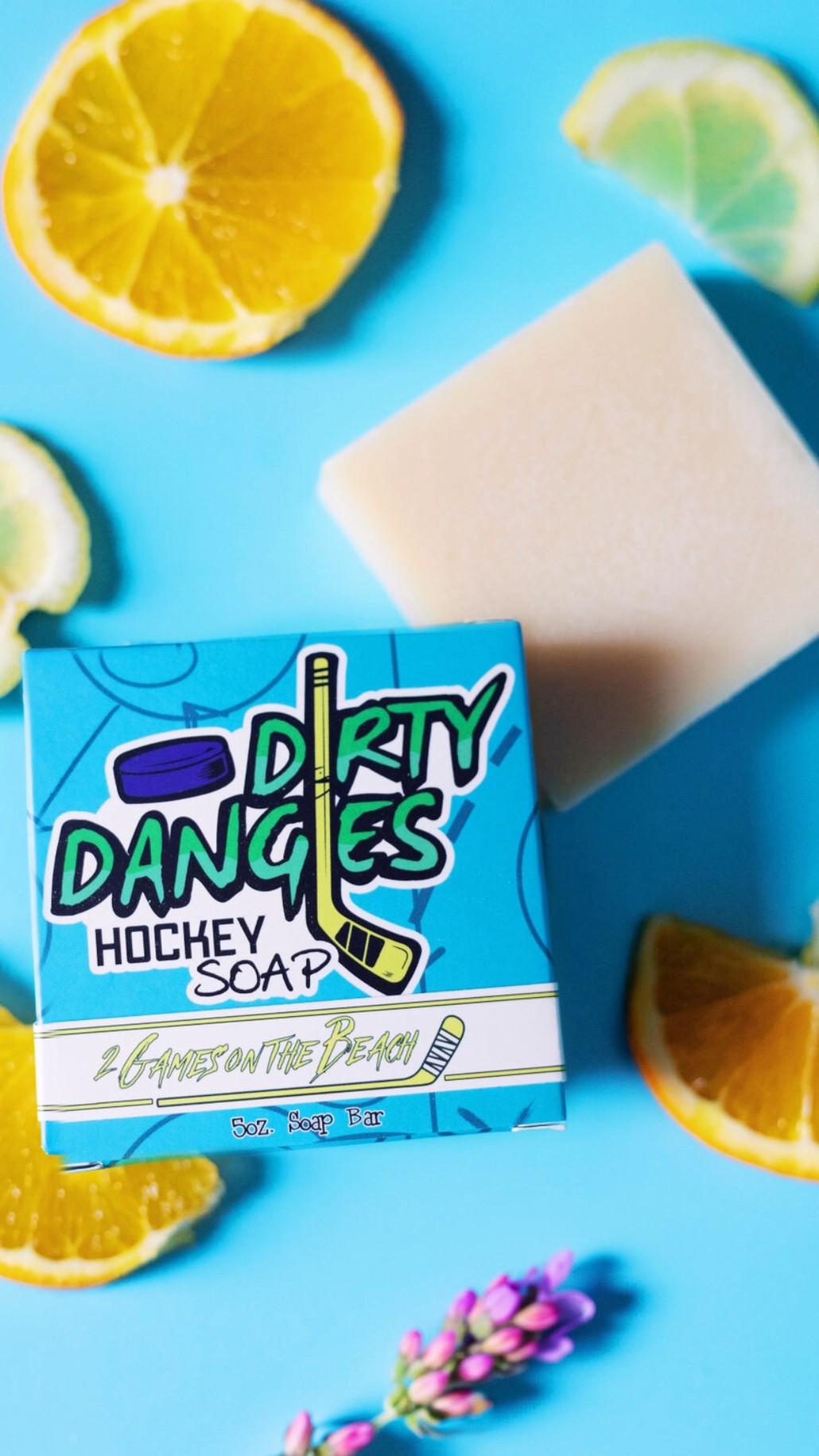 A yellow bar of dirty dangles hockey soap on a blue background with oranges lemons and lavender.