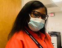 Professional woman in a red blazer and eyeglasses, with a face mask, possibly representing a satisfied Bella Terra Oils customer in a workplace setting, with office equipment in the background