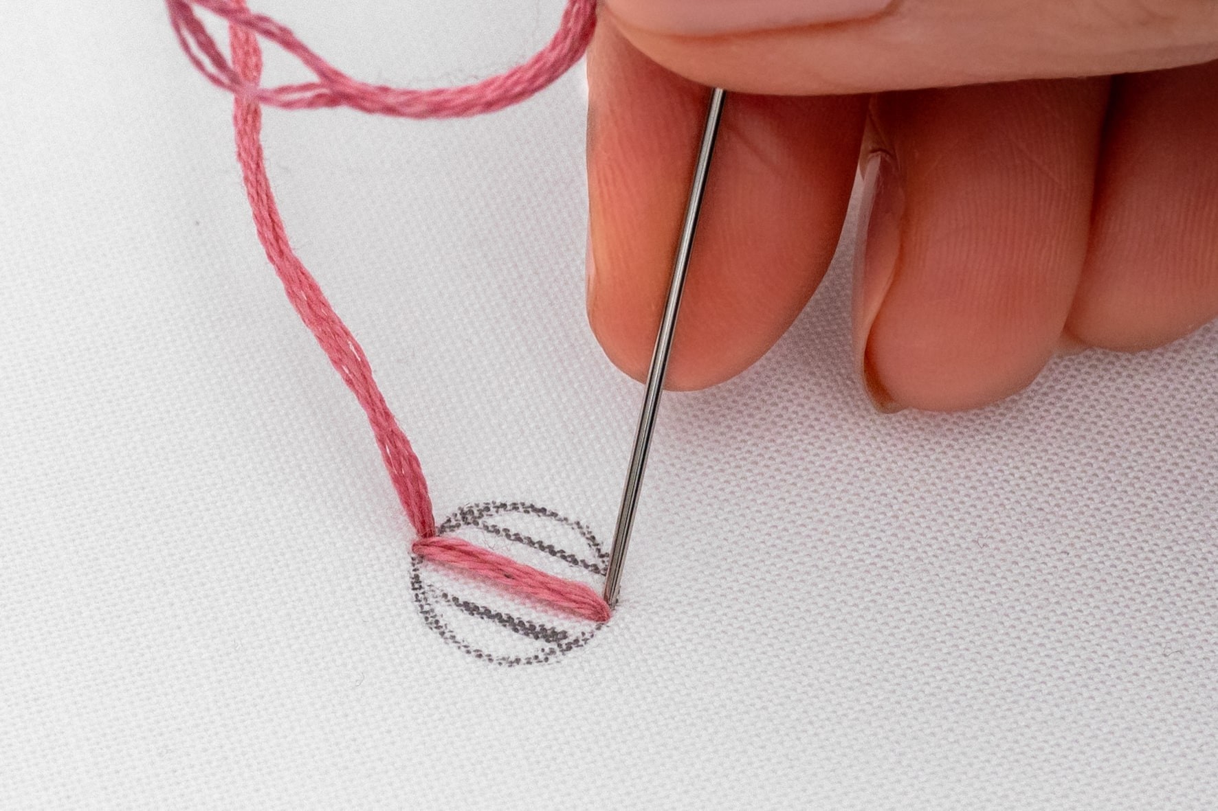 A needle pokes down next to a line of satin stitch.