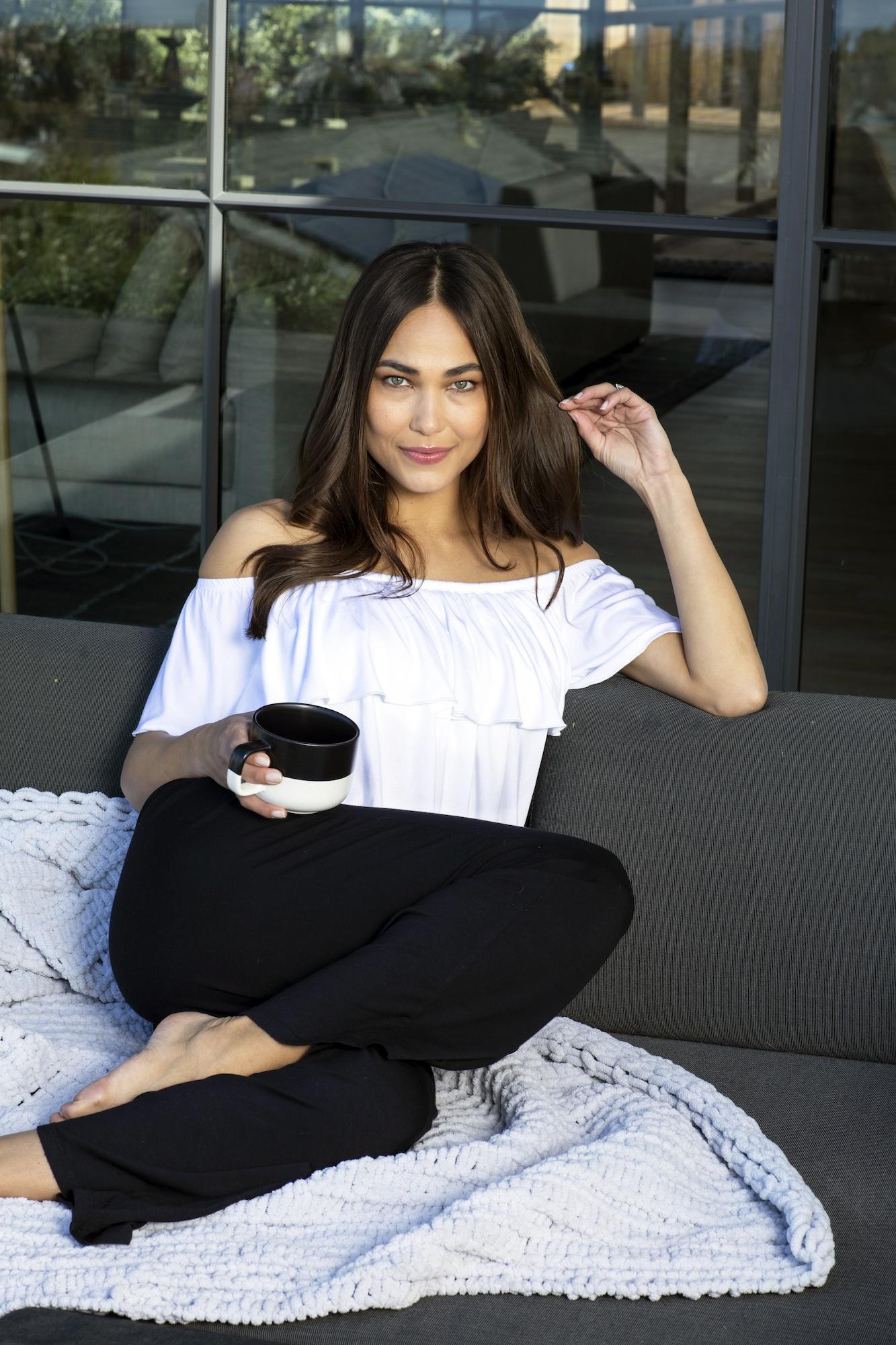 Woman lounging on outdoor couch with coffee wearing the white flirt top