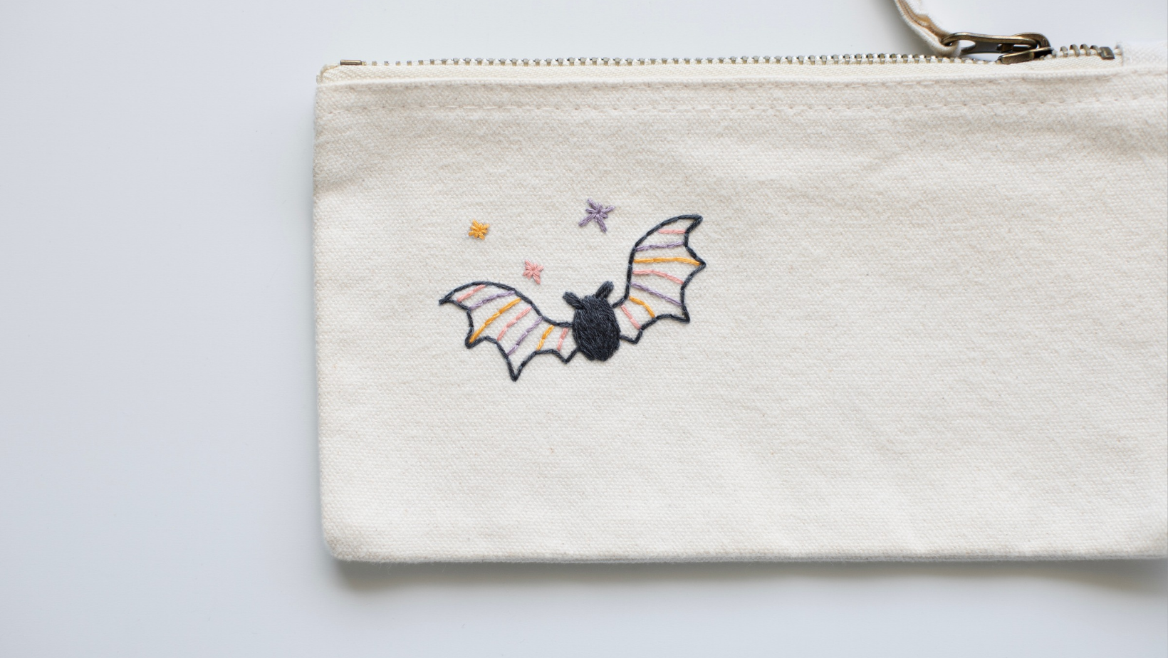 A bat with striped wings embroidered onto a cream canvas pencil pouch.