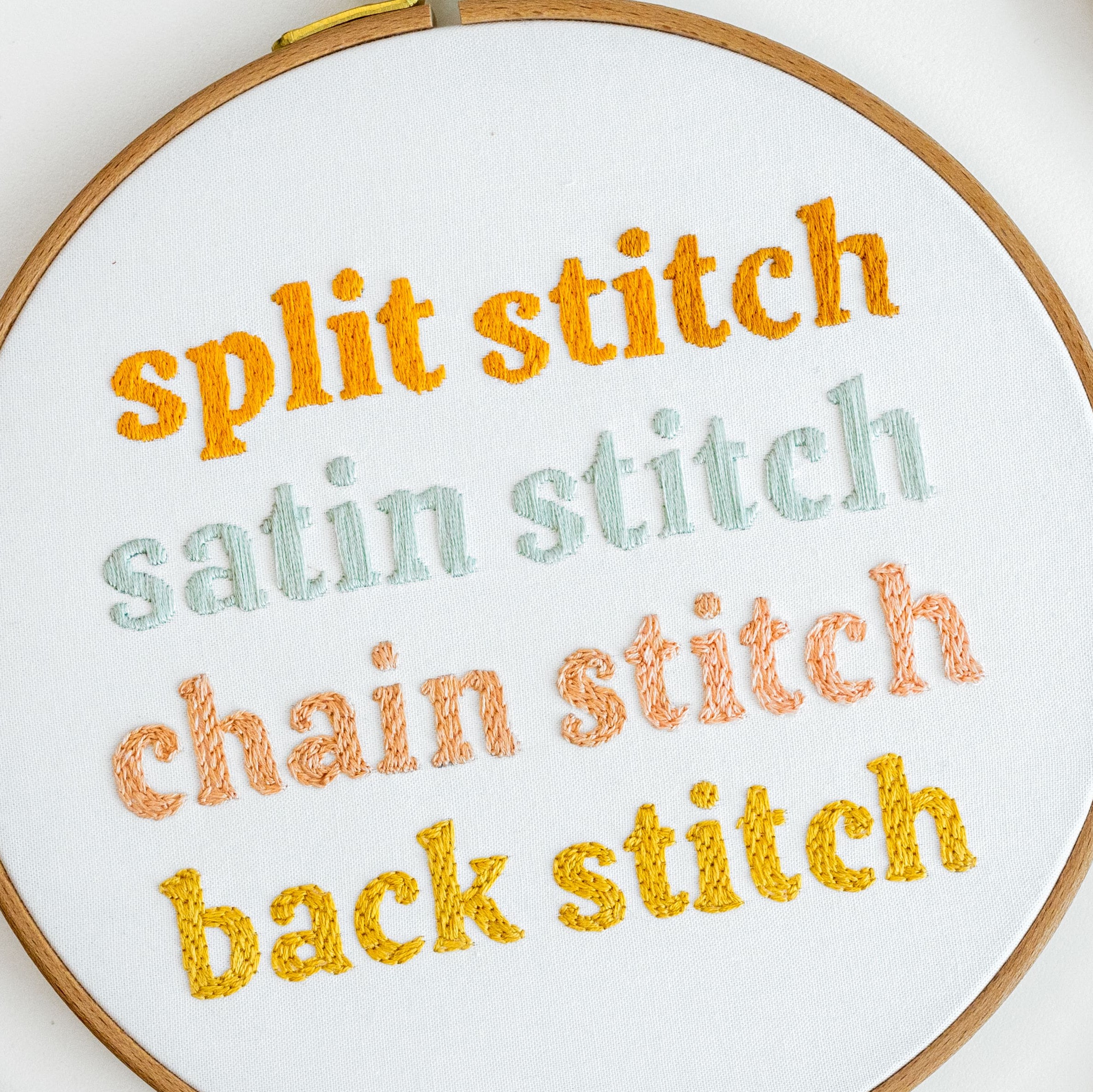 Words are stitched on an embroidery hoop with split stitch, satin stitch, chain stitch, and back stitch.