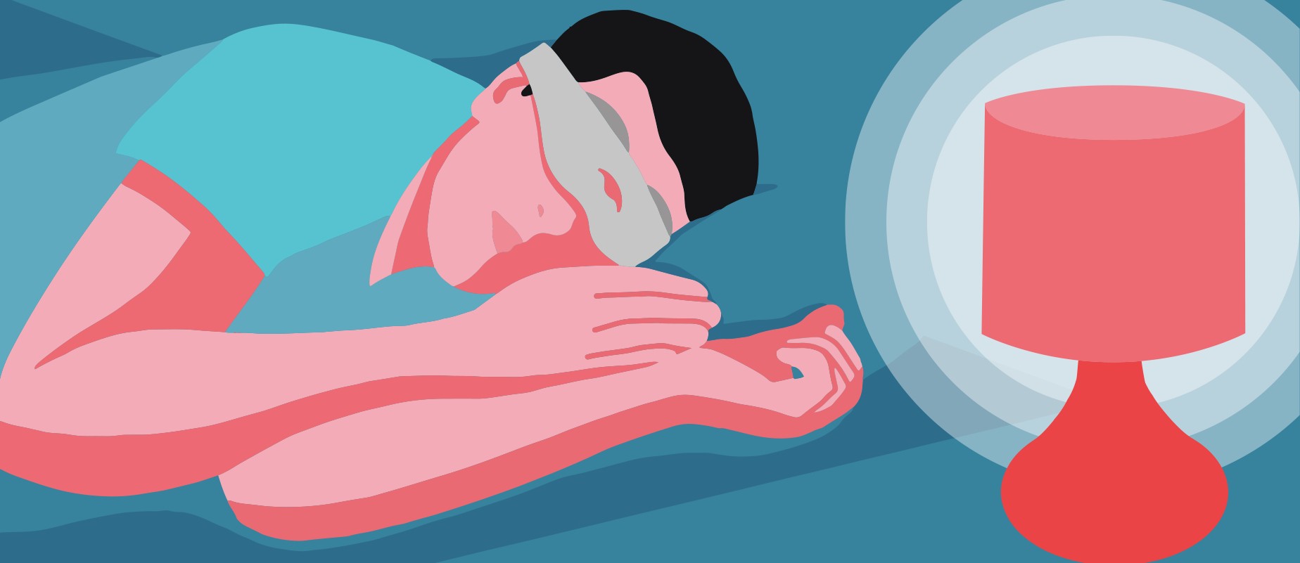 A man lying in bed wearing a sleep mask to block out light from his table lamp.