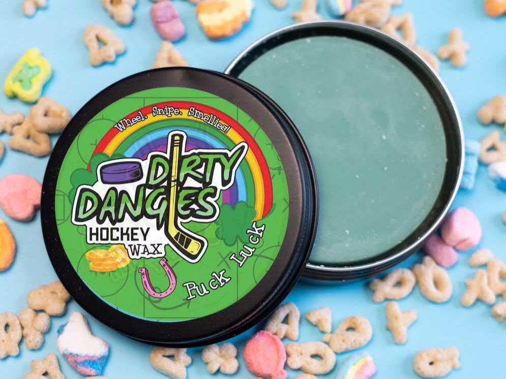 A tin of Dirty Dangles Hockey Wax Puck Luck St Patrick's Day scent on a blue background with lucky breakfast cereal