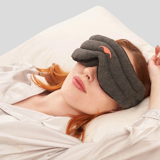 A pretty girl with red hair lying on a pillow and wearing a weighted sleep mask from Manta Sleep.