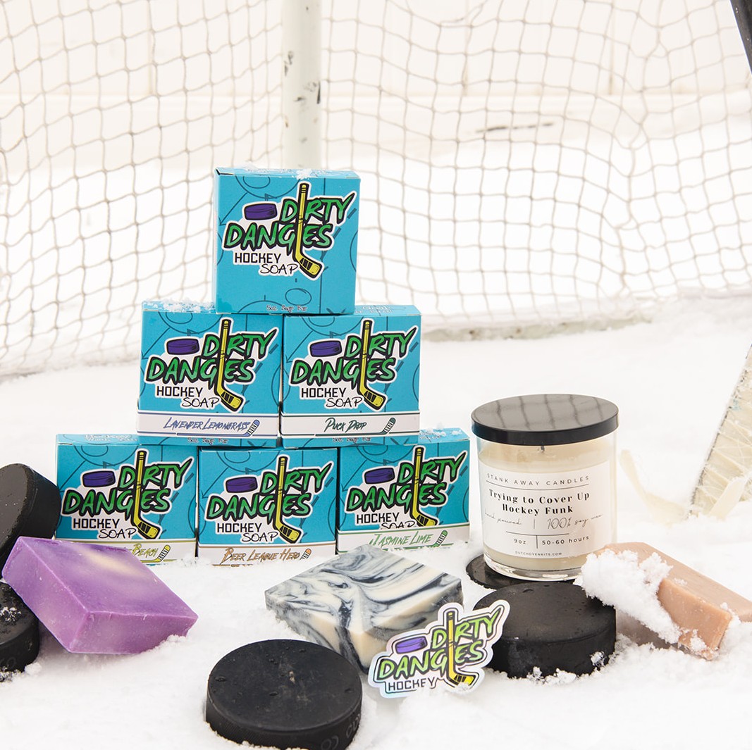 6 Soap bars in a stack with a purple soap, a black & white soap and a candle on a snowy hockey background.