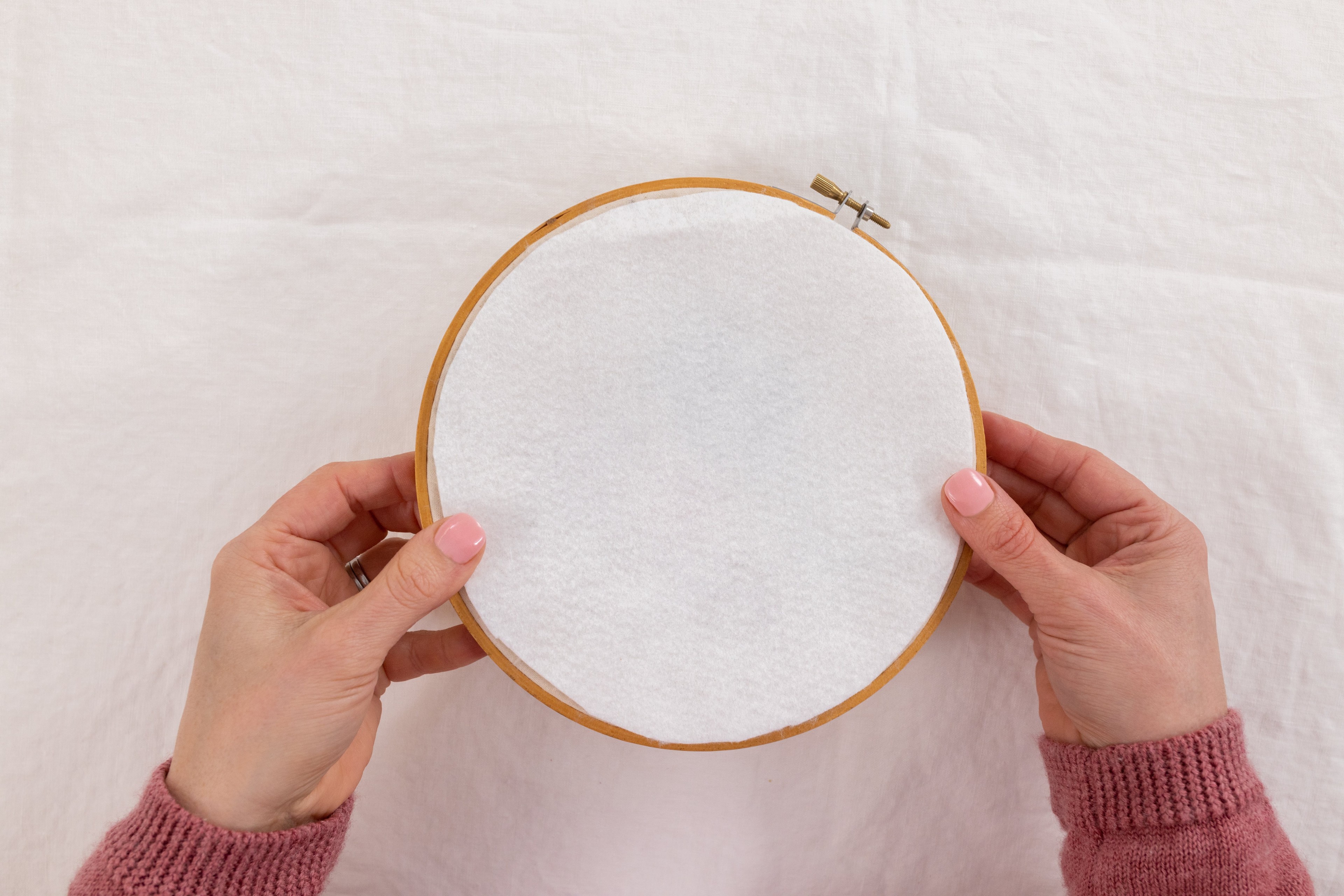 A hand holds a fabric backing over the back of the hoop.