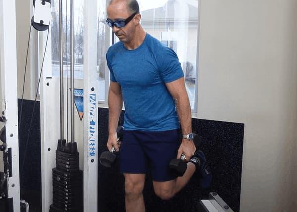 Man In Blue with Shorts Holding Dumbbells in Gym Outside View