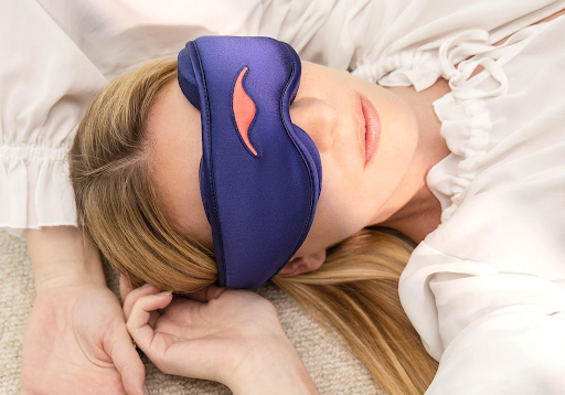 A blonde girl lying down wearing a silk sleep mask for night shift workers.